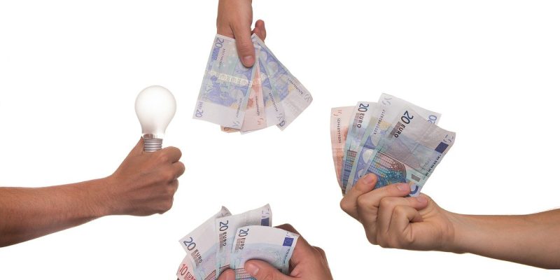 One hand holding a light bulb and three others holding Euro money
